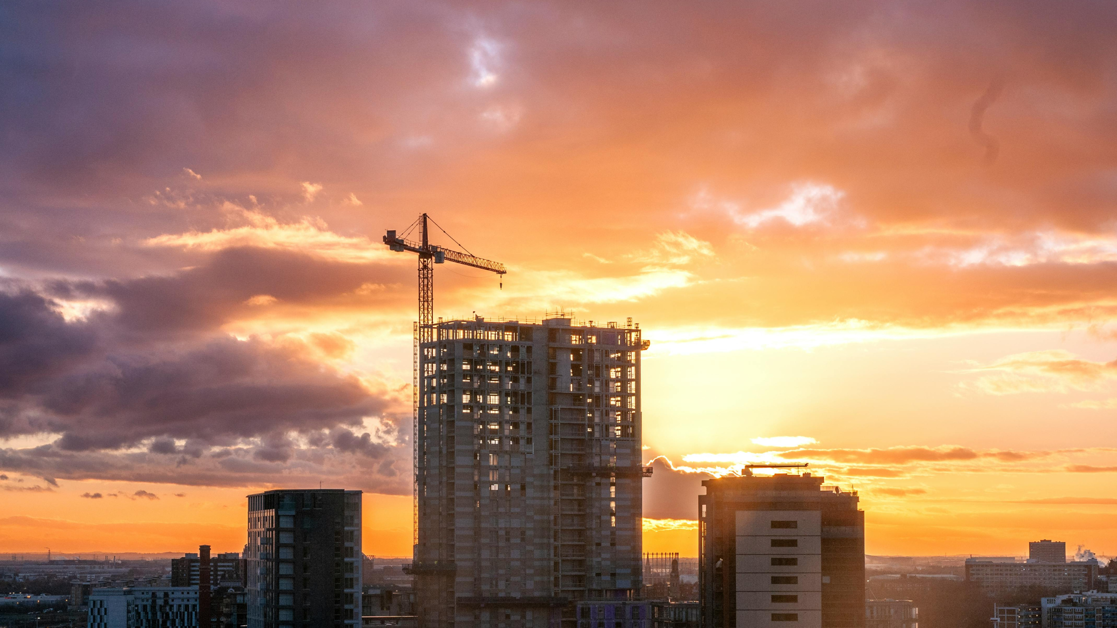 High-rise building under construction with a tower crane at sunset, representing the impact of strong leadership on construction quality and project success.