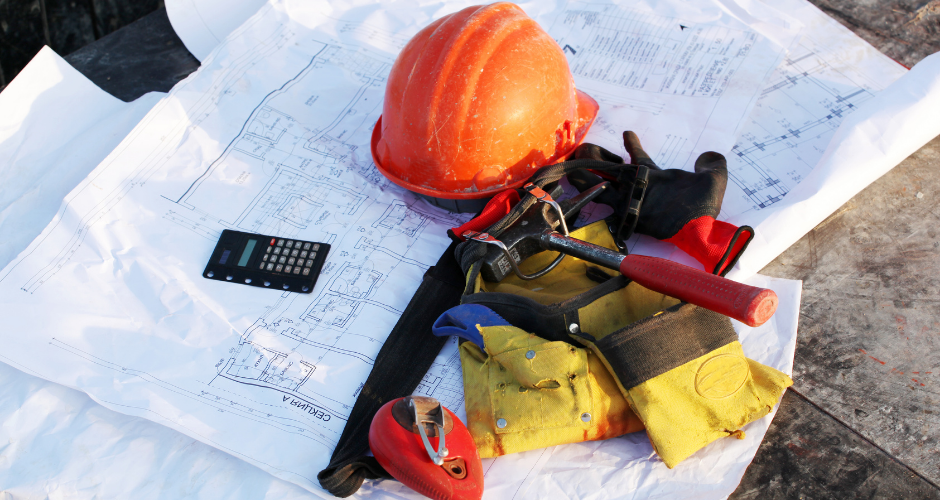 Construction blueprints laid out with a hard hat, tools, and calculator, representing the planning and coordination required for successful building projects.