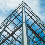 Upward view of a steel building frame against the sky, emphasizing the structural precision and engineering involved in modern construction.