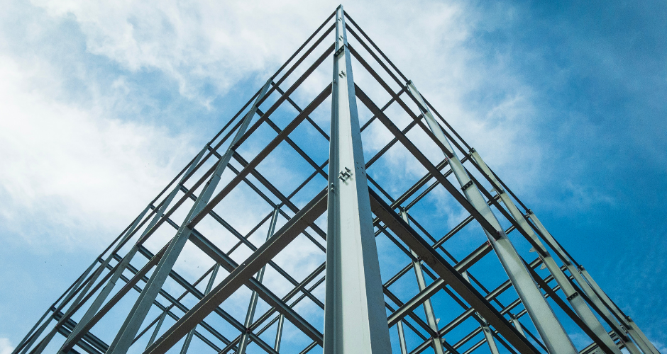 Upward view of a steel building frame against the sky, emphasizing the structural precision and engineering involved in modern construction.