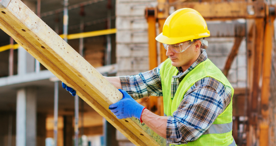 Construction worker in protective gear lifting and positioning a large wooden beam at an active jobsite.